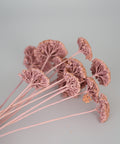 A bouquet of dried decorative flowers with delicate pink stems and clustered round, textured blooms, arranged on a plain light gray background.